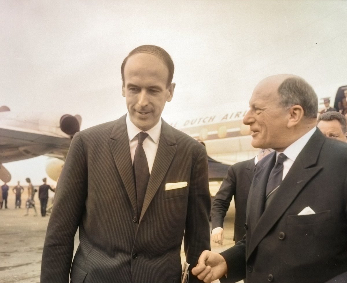 Valéry Giscard d'Estaing in a dark suit and glasses, stepping from an aircraft doorway onto airstairs.